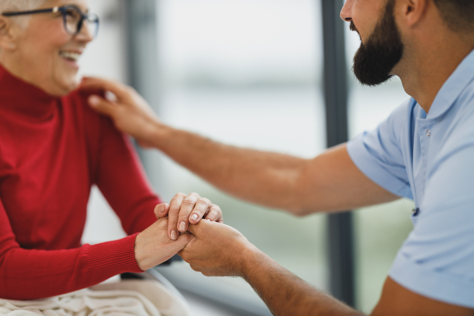 Un aidant tient chaleureusement les mains d'une dame âgée souriante